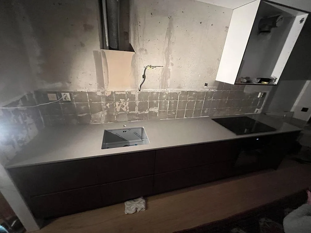 Köksbänkskiva i polerad Technistone Noble Concrete Grey med underlimmad rostfri diskho, svart induktionshäll och mosaikstänkskydd under montering i Västerås.