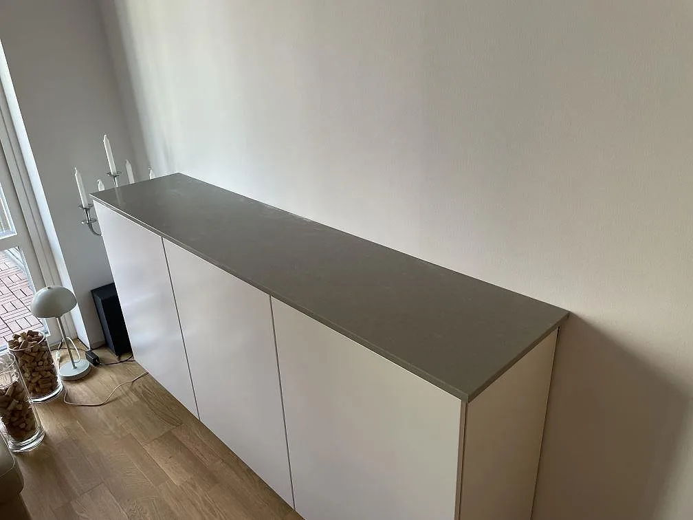 Lång bänkskiva i Technistone Noble Concrete Grey, polerad kvartskomposit, monterad på vit förvaring vid fönster i Västerås.