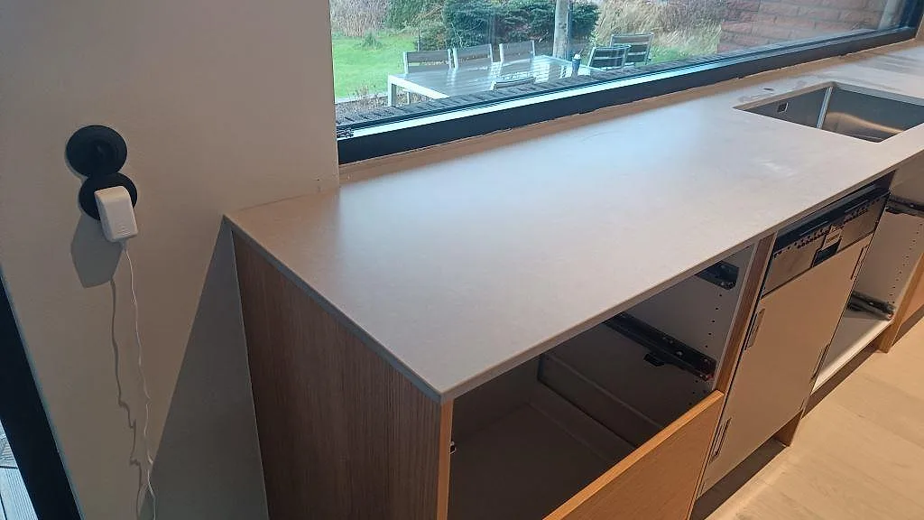 Lång köksbänkskiva i matt Technistone Noble Concrete Grey längs fönster med rostfri diskho synlig i Västra Frölunda.