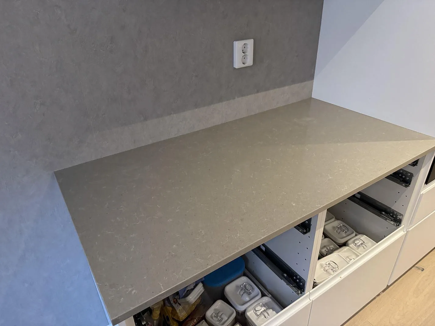 Lång väggbänkskiva i polerad Technistone Noble Concrete Grey med låg stänkkant och öppna köksstommar i Västra Frölunda.