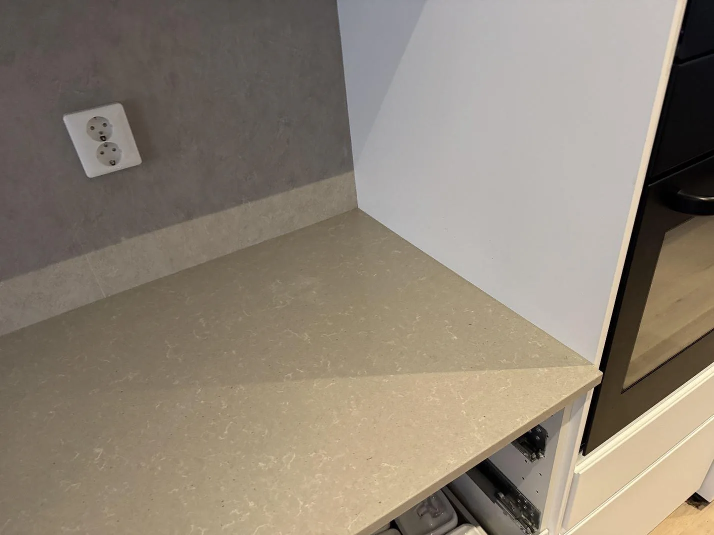 Hörndetalj av köksbänkskiva i polerad Technistone Noble Concrete Grey med låg uppvikt kant intill ugn i Västra Frölunda.