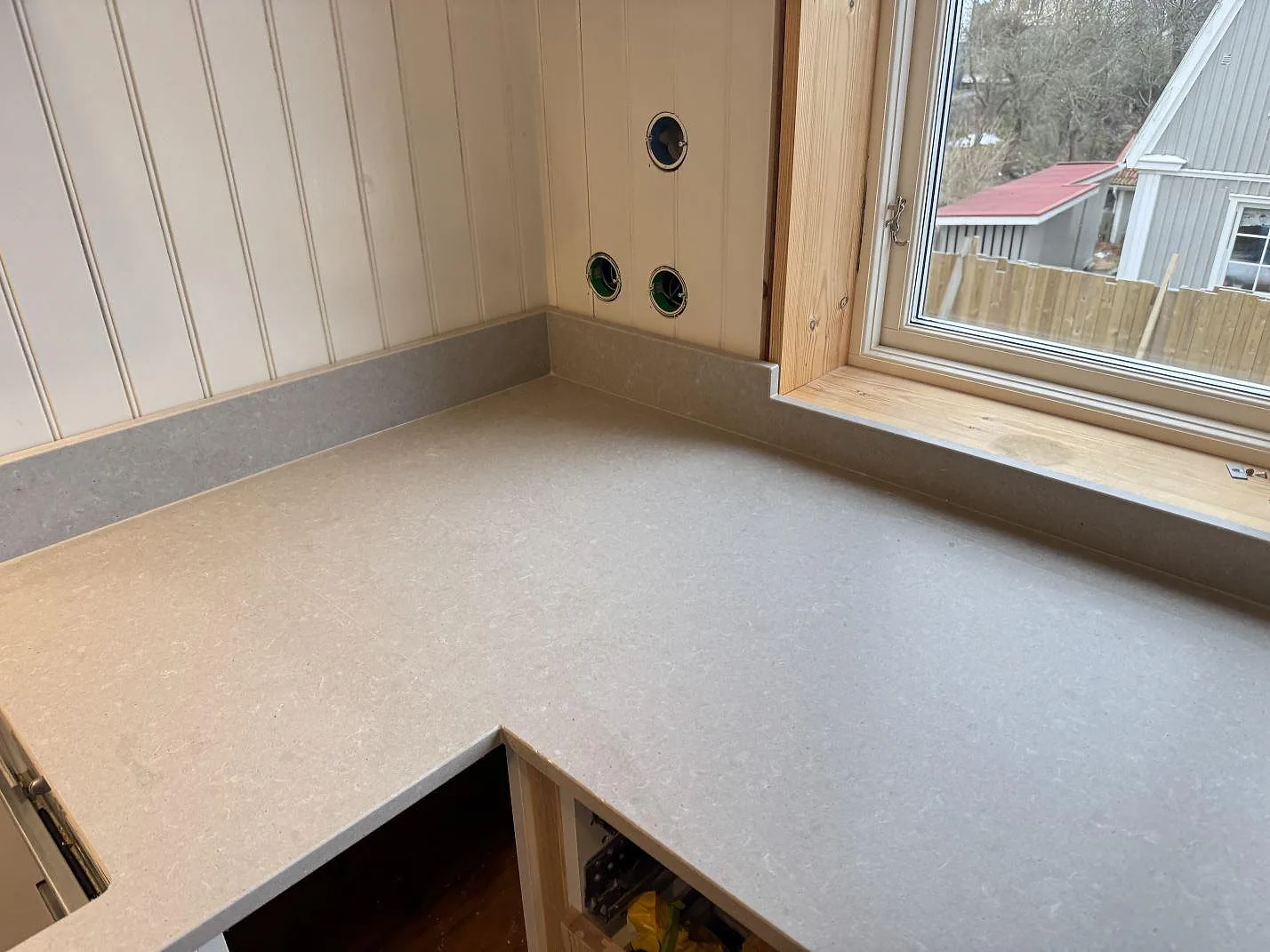 Grå betongliknande köksbänkskiva i Technistone Noble Concrete Grey med uppvikt stänkkant mot fönsterbänken i ett kök i Västra Frölunda.