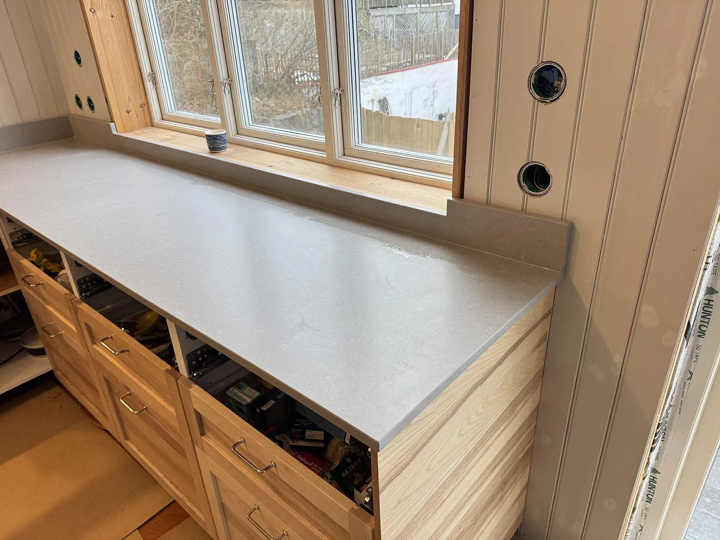 Matt grå köksbänkskiva i Technistone Noble Concrete Grey med uppvikt stänkkant över ljusa stommar i ett kök under montering i Västra Frölunda.