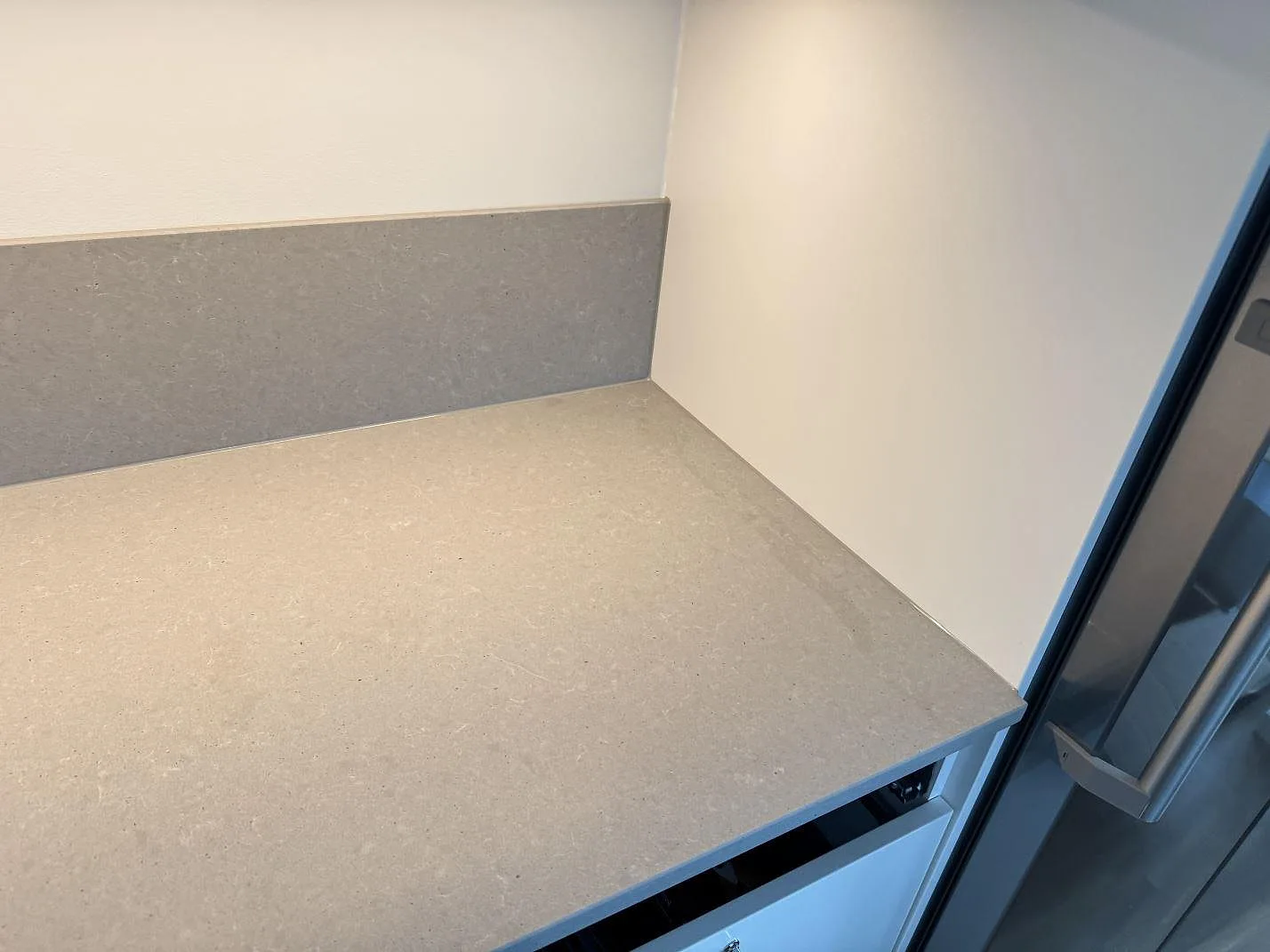 Grå köksbänkskiva i matt Technistone Noble Concrete Grey som möter ett rostfritt kylskåp i ett kök i Varberg.
