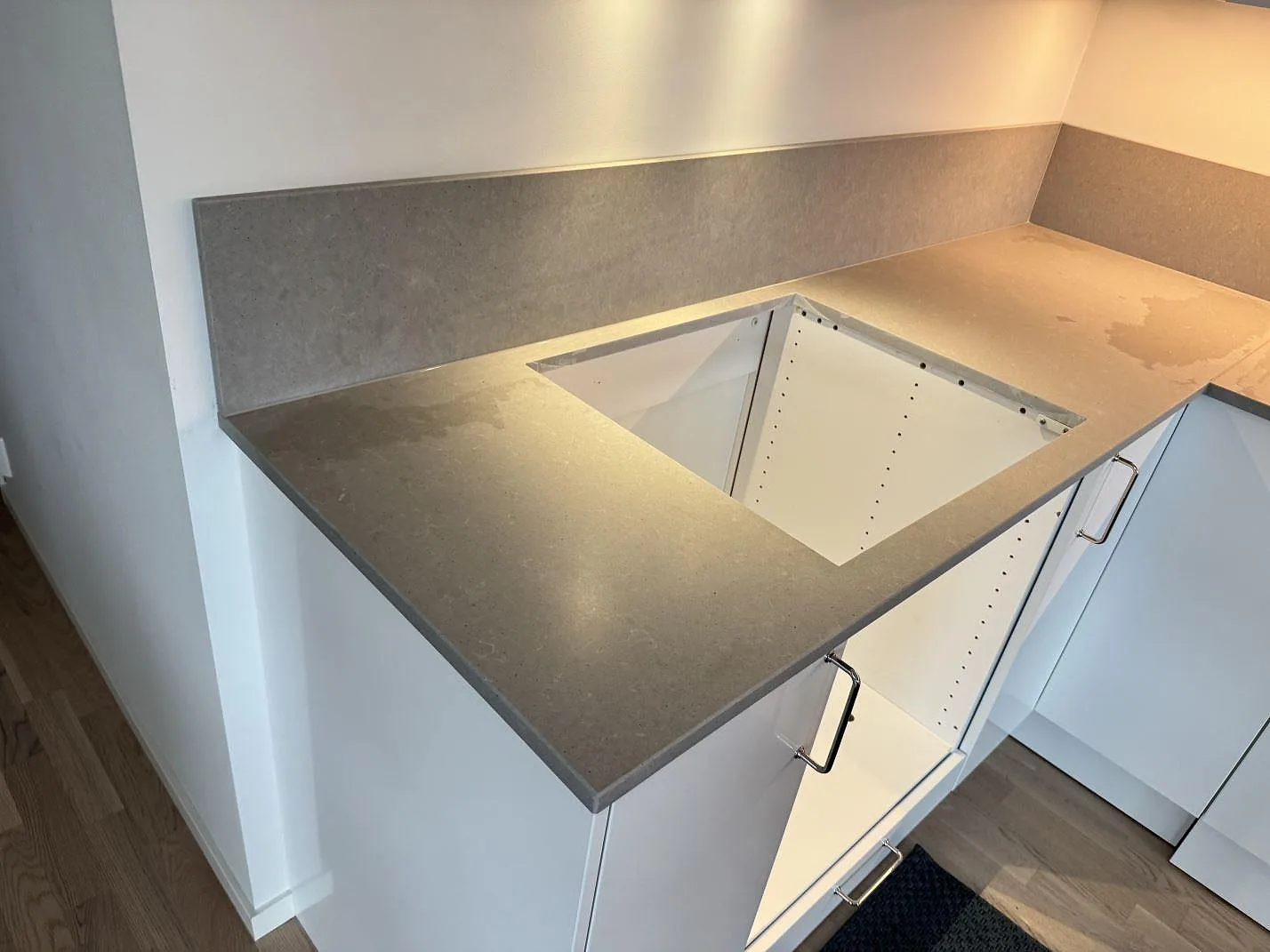 L-formad köksbänkskiva i matt Technistone Noble Concrete Grey runt ett hörn med uppvikt stänkkant och öppna köksstommar i Varberg.