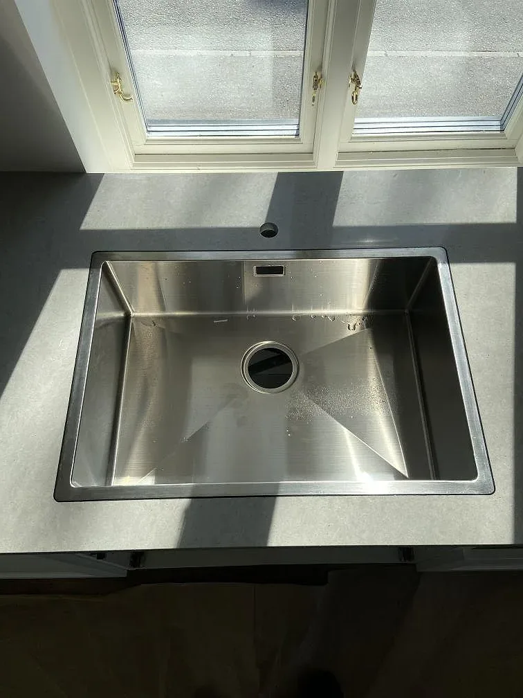 Underlimmad rostfri diskho i matt betonggrå Technistone Noble Concrete Grey bänkskiva under ett fönster i ett kök i Vellinge.