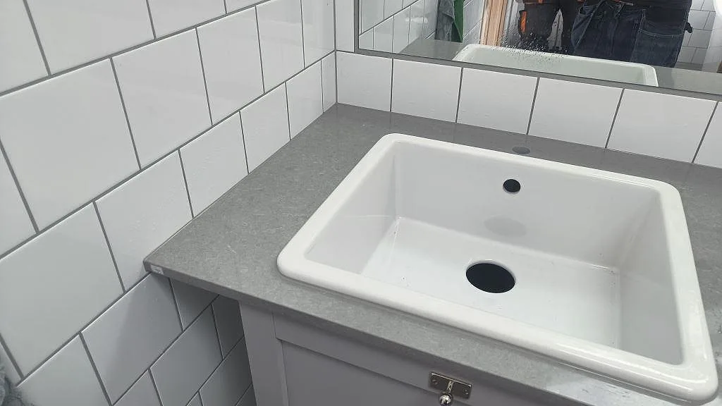 Närbild på polerad Technistone Noble Concrete Grey komposit runt en vit ho i en tvättstuga i Vellinge.