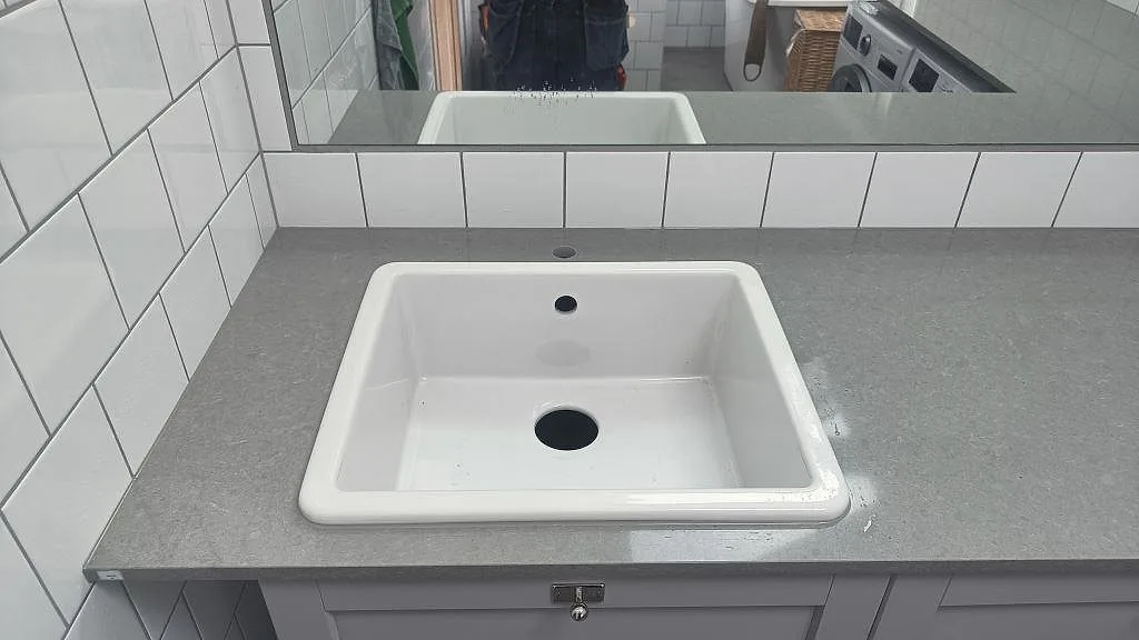 Vit ho monterad ovanpå en polerad Technistone Noble Concrete Grey bänkskiva i tvättstuga i Vellinge.