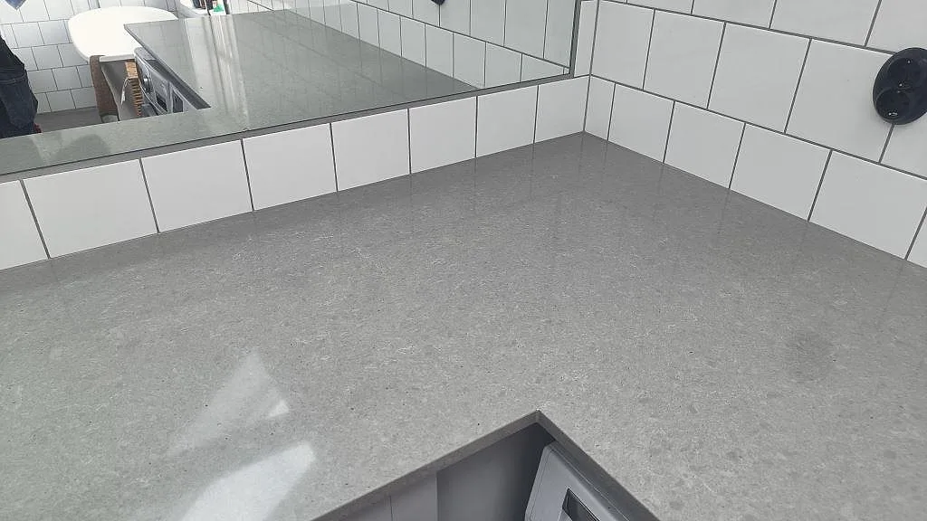 Lång arbetsbänk i polerad Technistone Noble Concrete Grey komposit över tvättmaskin och torktumlare i Vellinge.
