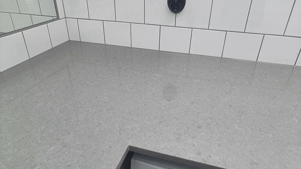 Närbild på den polerade grå kompositytan Technistone Noble Concrete Grey mot vita kakelplattor i Vellinge.
