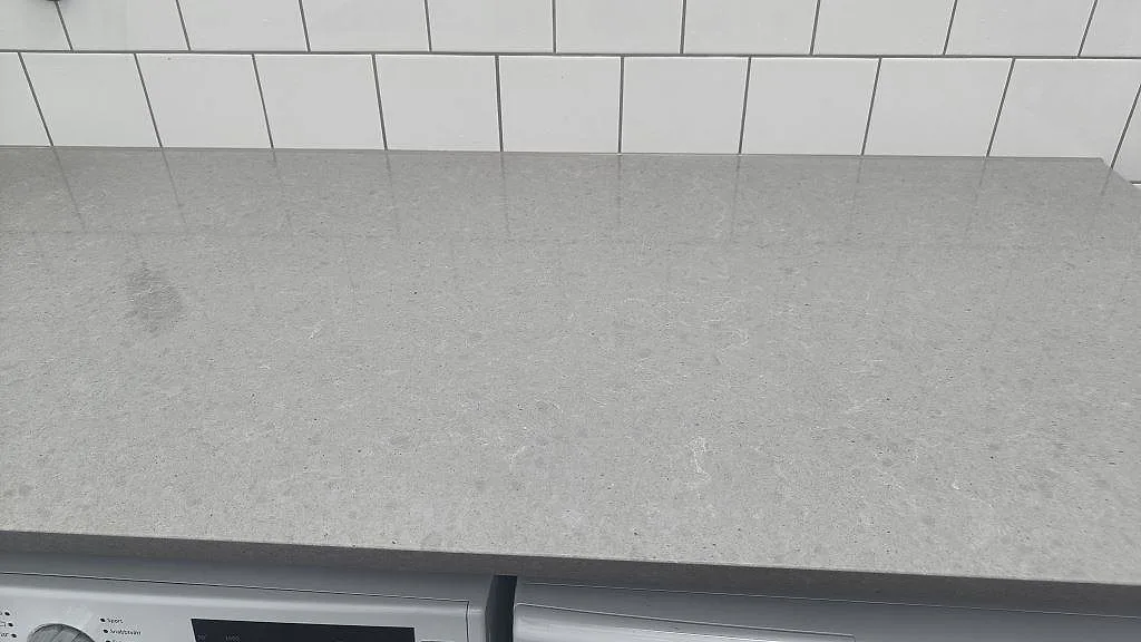Rak vy över arbetsbänk i polerad Technistone Noble Concrete Grey komposit ovanför tvättmaskin och torktumlare i Vellinge.