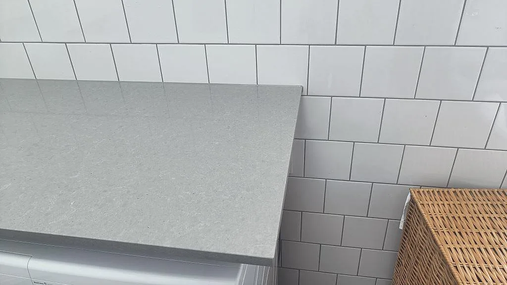 Avslut på tvättbänk i polerad Technistone Noble Concrete Grey komposit mot vitt kakel i Vellinge.