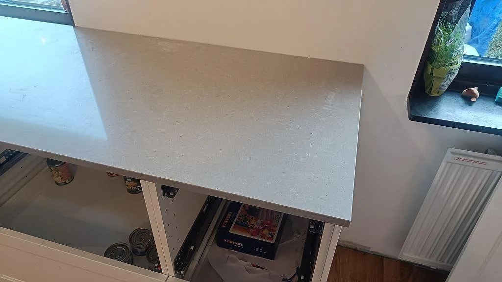 Ljusgrå Technistone Noble Concrete Grey köksbänkskiva i polerad komposit vid fönster och vita stommar i Vellinge.
