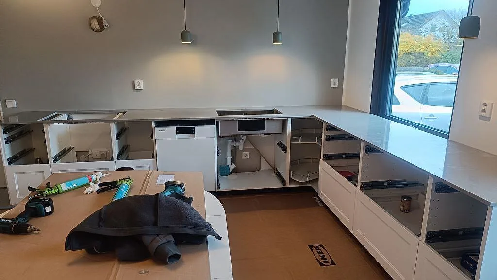 Köksbänkskiva i ljusgrå Technistone Noble Concrete Grey, polerad komposit, monterad längs vita köksstommar i Vellinge.