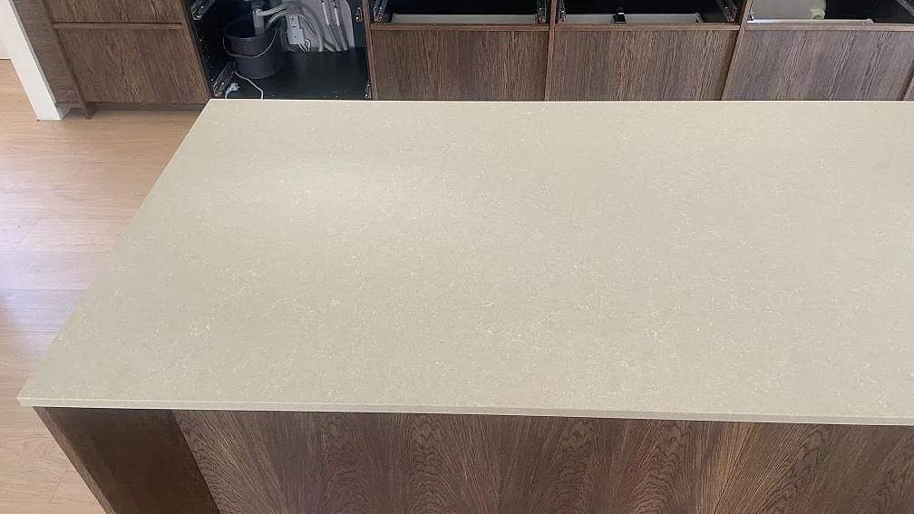 Stor köksö i polerad Technistone Noble Ivory White med varm ljus komposityta och öppna trästommar i köket i Åhus.