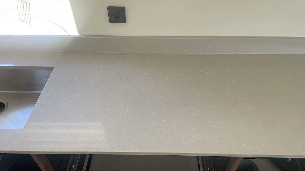 Närbild av polerad Technistone Noble Ivory White på väggbänken, ljus kvartskomposit med diskho och stänkkant under montering i Åhus.