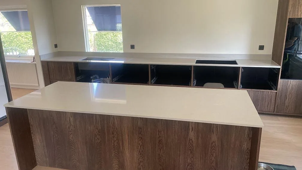 Köksbänkskiva och köksö i polerad Technistone Noble Ivory White, ljus kvartskomposit med häll och rostfri diskho i ett kök under montering i Åhus.