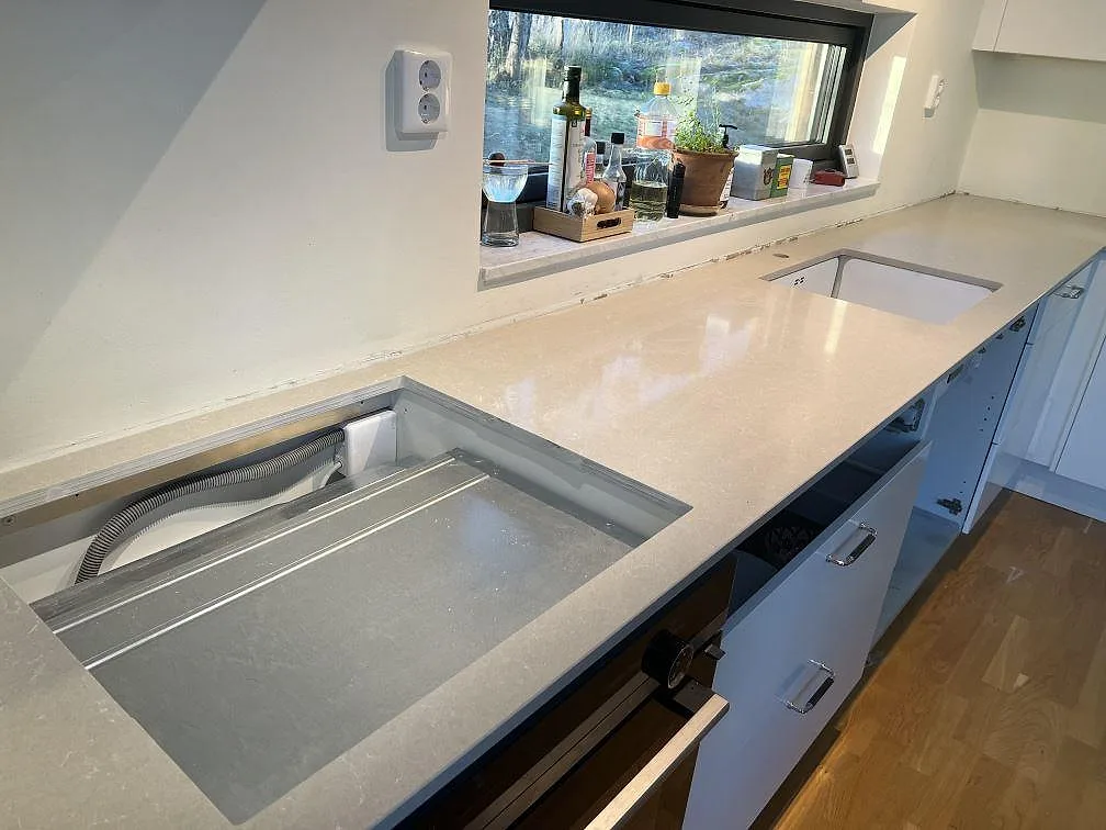 Närbild av polerad Technistone Noble Ivory White köksbänkskiva i vit kvartskomposit med synliga urtag i ett kök i Åkersberga.