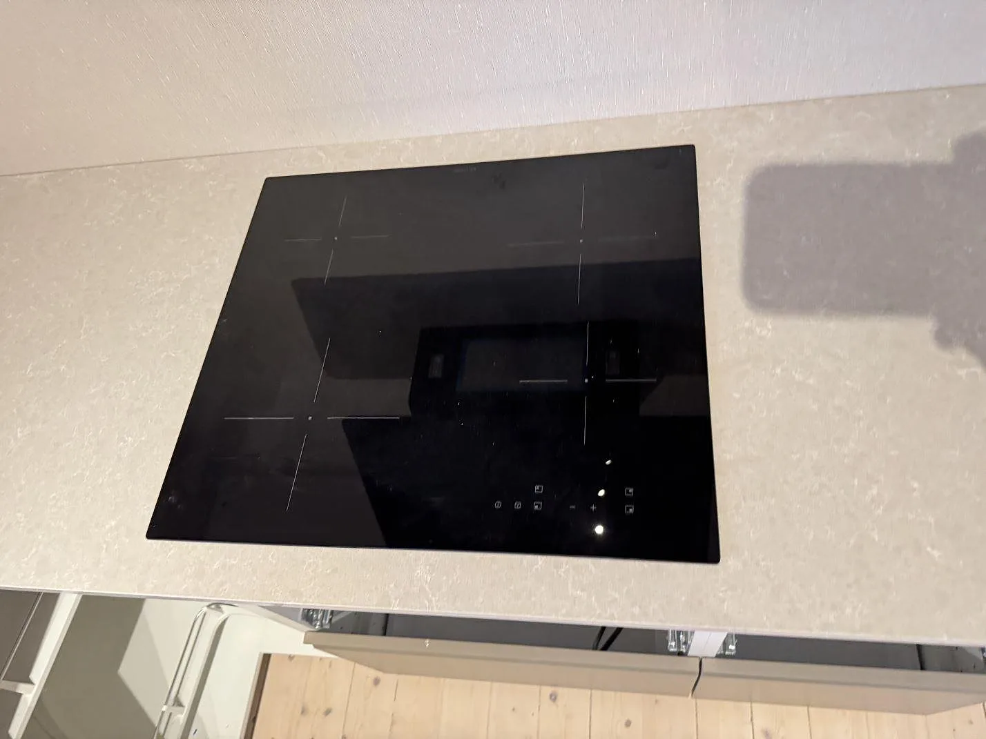 Detalj av svart häll placerad i polerad köksbänkskiva av Technistone Noble Ivory White i Ängelholm.