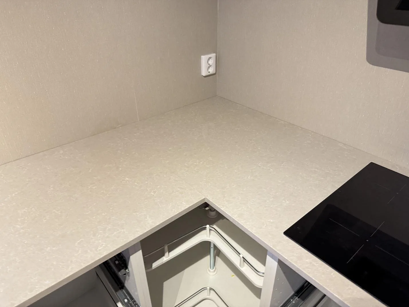 Hörnparti av köksbänkskiva i Technistone Noble Ivory White, polerad komposit, med svart häll och ljus ådring i Ängelholm.