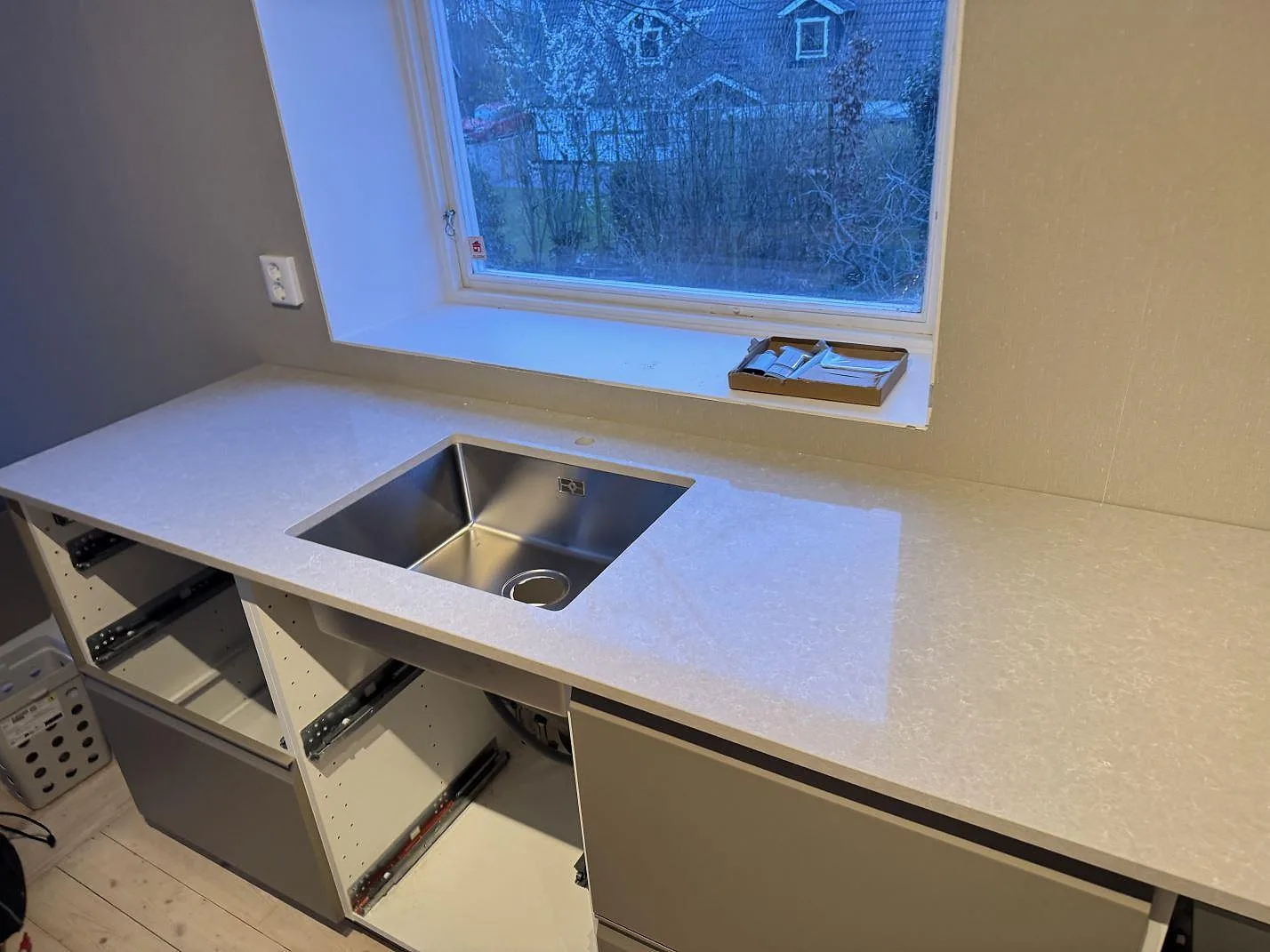 Polerad köksbänkskiva i Technistone Noble Ivory White med rostfri diskho, låg stänkkant och fönsternisch i kök i Ängelholm.