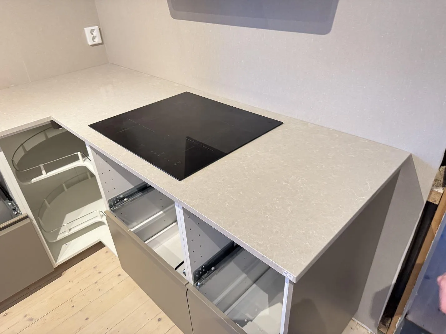 L-formad köksbänkskiva i Technistone Noble Ivory White, polerad komposit, med svart häll och öppna stommar under montering i Ängelholm.