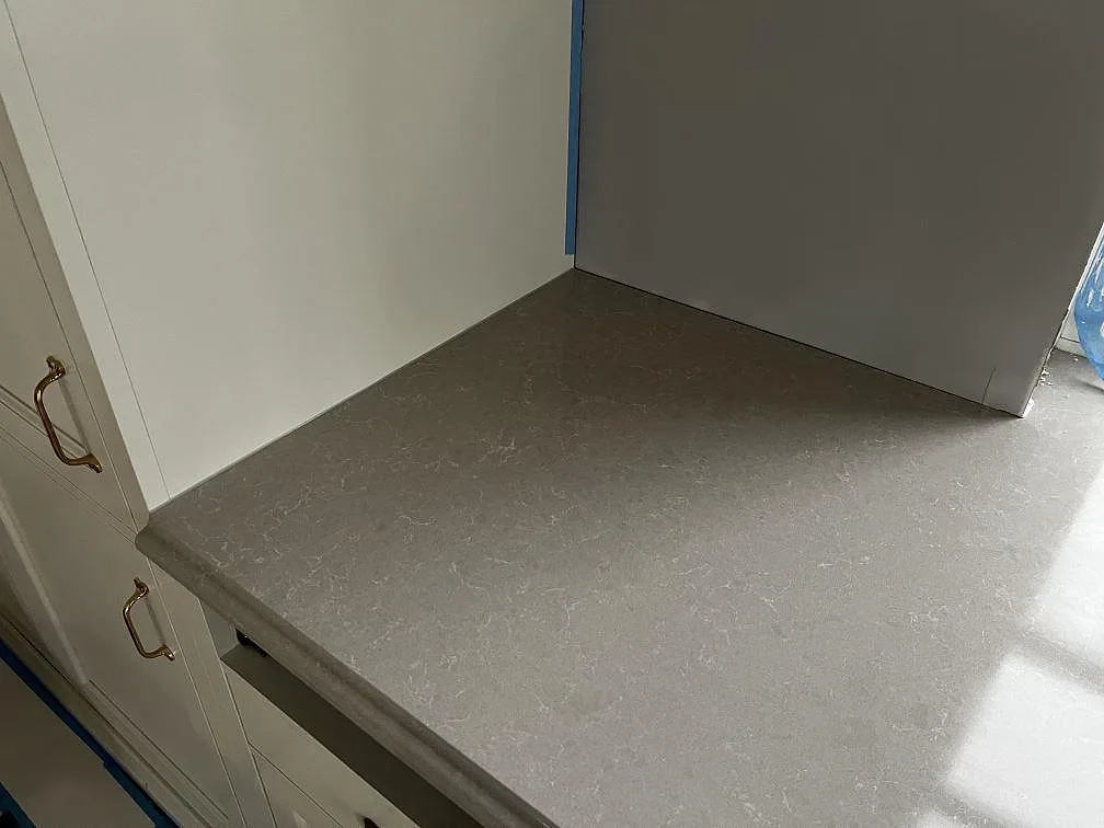 Detalj av polerad Technistone Noble Ivory White i ett kökshörn med vit inredning och synlig gråvit mönstring i Barsebäck.