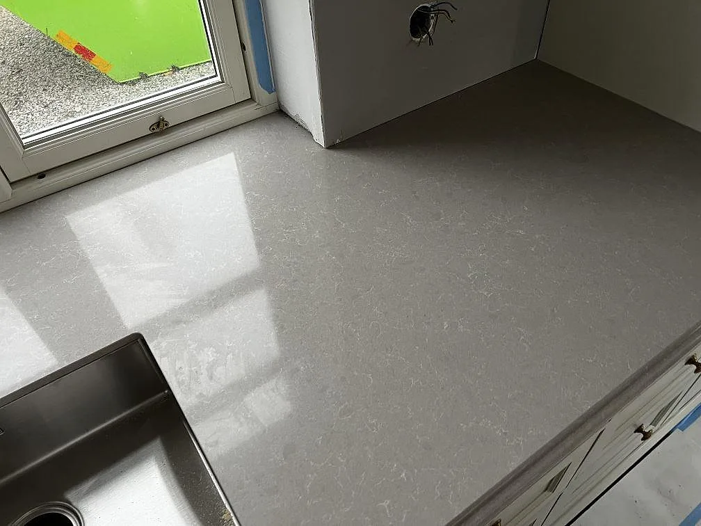 Bänkyta vid fönster i polerad Technistone Noble Ivory White med diskho och ljusreflexer under montering i Barsebäck.