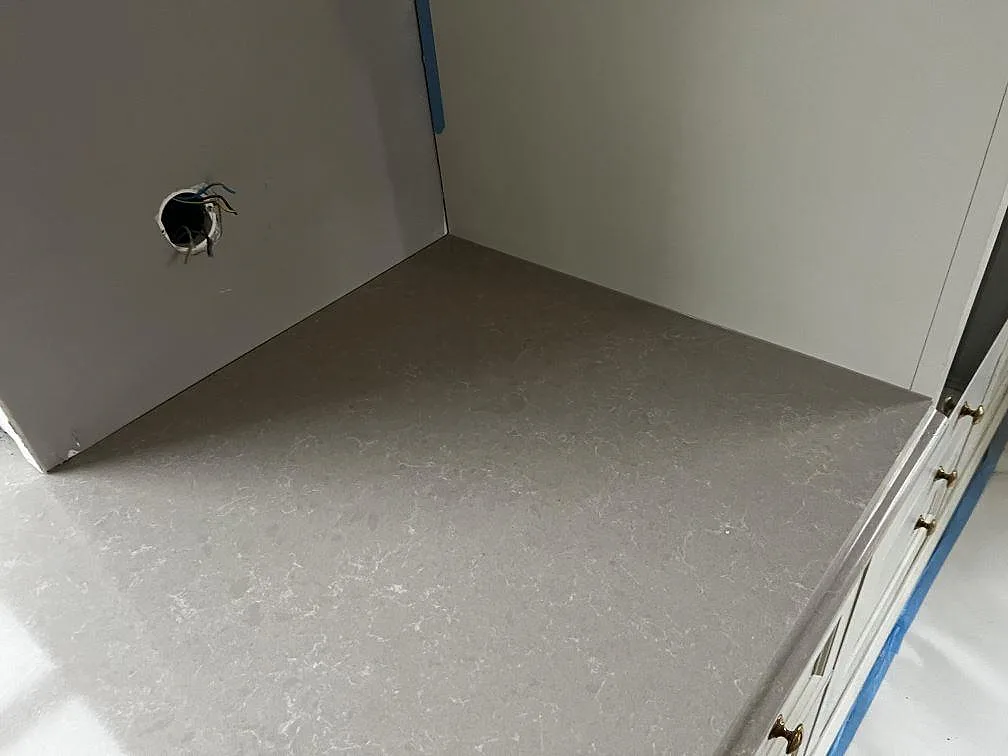 Sidobänk i polerad Technistone Noble Ivory White intill högskåp och vägg under köksmontering i Barsebäck.