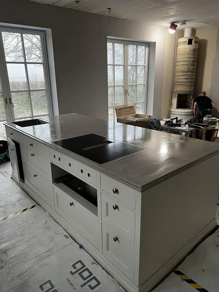 Köksö i 30 mm polerad Technistone Noble Ivory White med svart häll och vita luckor under montering i Barsebäck.