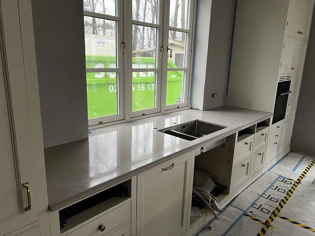 Köksbänkskiva i Technistone Noble Ivory White, polerad kvartskomposit, med underlimmad dubbelho och stora fönster i ett kök i Barsebäck.
