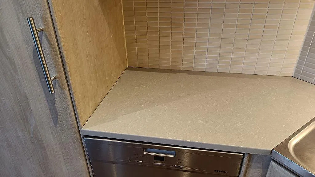 Polerad Technistone Noble Ivory White bänkskiva i komposit över diskmaskin med rak framkant i ett kök i Bjuv.