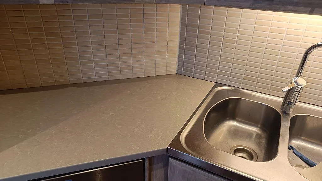Närbild på ljus kompositbänkskiva i Technistone Noble Ivory White som möter rostfri dubbelho och kakel i kök i Bjuv.