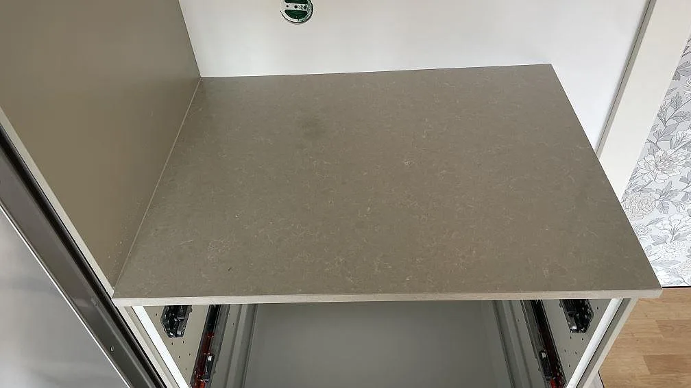 Sidobänk i polerad Technistone Noble Ivory White, kvartskomposit, monterad mot vägg och kyl i ett kök i Dalsjöfors.