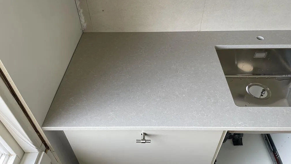 Vänster del av köksbänkskiva i polerad Technistone Noble Ivory White med rostfri diskho och blandarhål i Dalsjöfors.