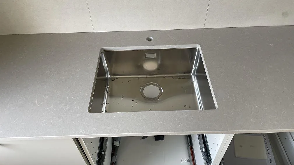 Närbild på rostfri diskho i en polerad köksbänkskiva i Technistone Noble Ivory White, kvartskomposit i Dalsjöfors.