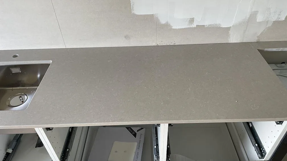 Detalj av polerad Technistone Noble Ivory White på köksbänk i Dalsjöfors, med diskho till vänster och hälluttag till höger.