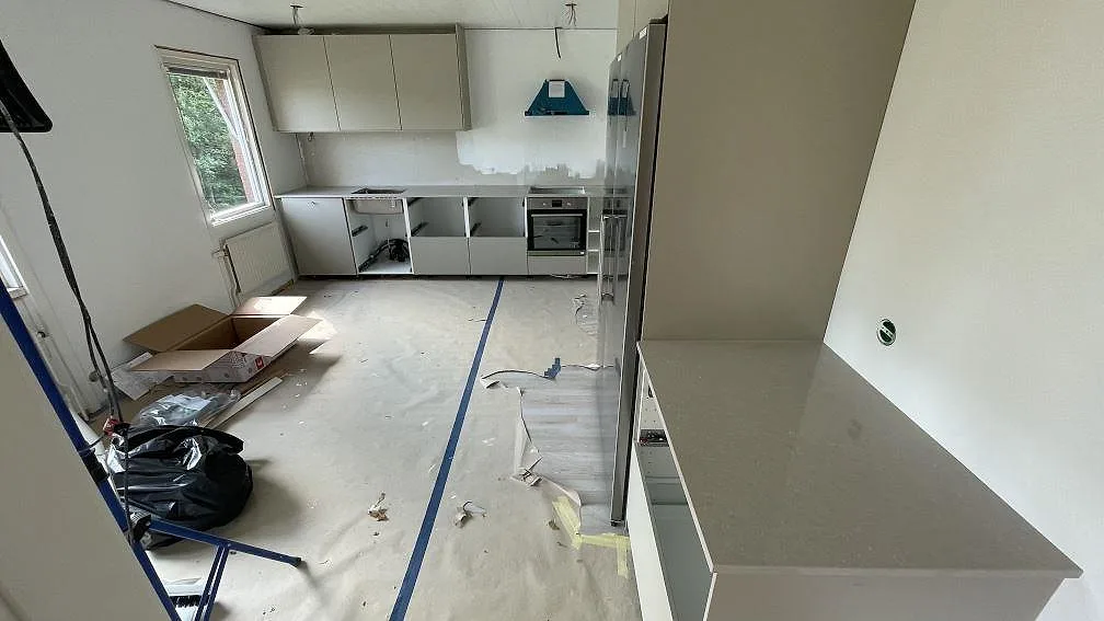 Översikt av kök under montering i Dalsjöfors med polerad köksbänkskiva i Technistone Noble Ivory White på både sidobänk och väggbänk.