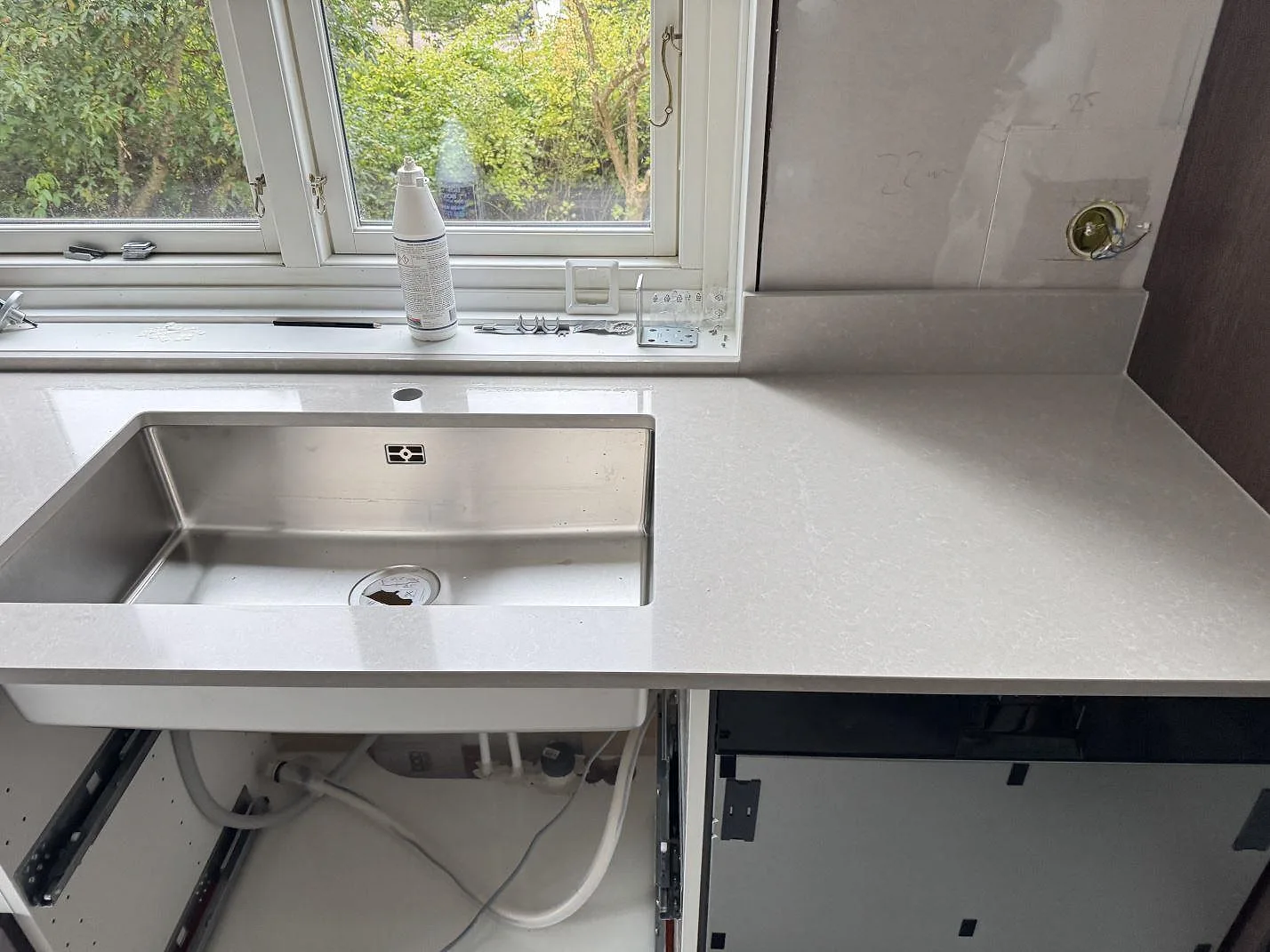 Köksbänkskiva i polerad Technistone Noble Ivory White komposit vid fönster, med rostfri diskho och stänkkant i ett kök i Eksjö.
