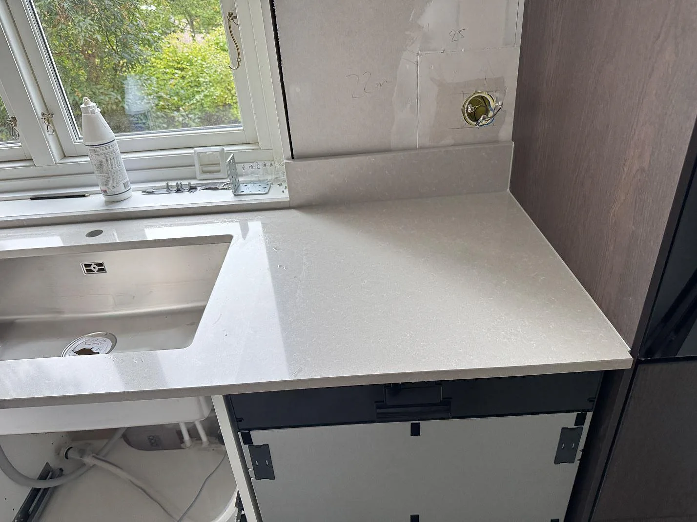 Närbild av polerad köksbänkskiva i Technistone Noble Ivory White komposit med rostfri diskho, stänkkant och fönster i Eksjö.