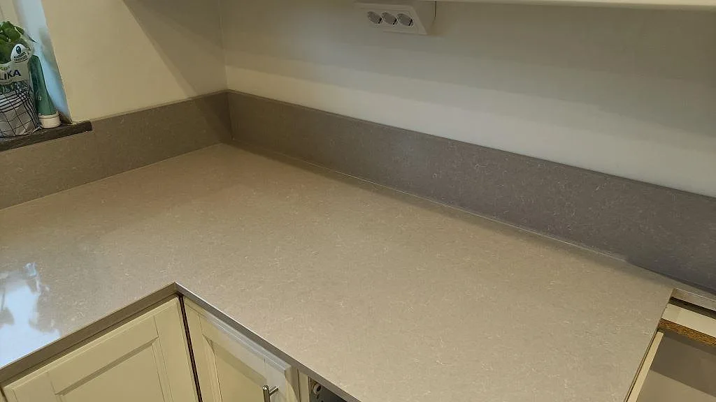 Hörnvy av ljus polerad Technistone Noble Ivory White på köksbänk med uppvikt stänkkant och synlig stenstruktur i Eslöv.