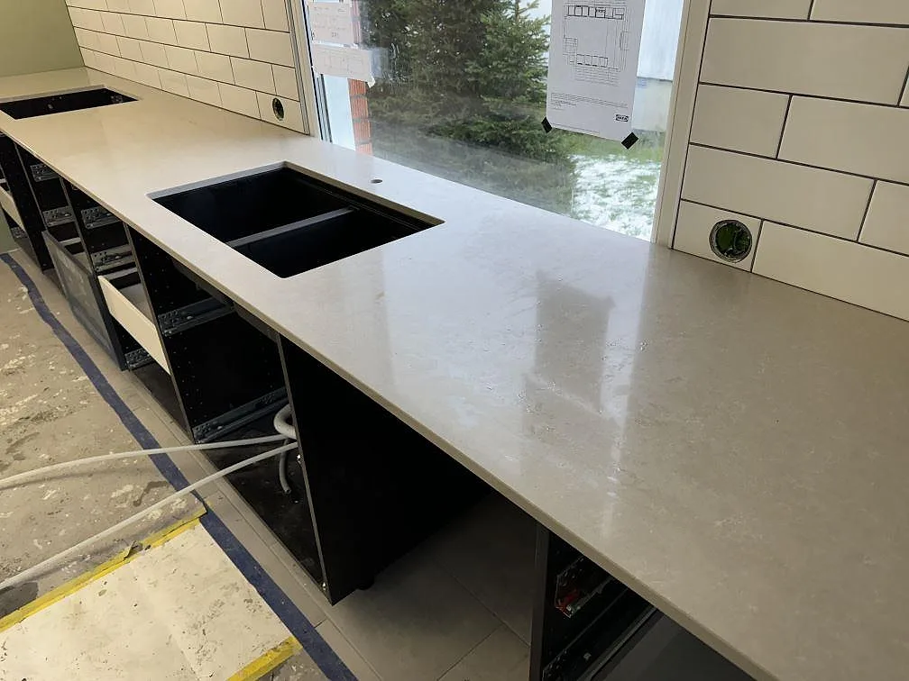 Polerad köksbänkskiva i Technistone Noble Ivory White med svart dubbelho, hällöppning och vitt kakel under montering i Falköping.