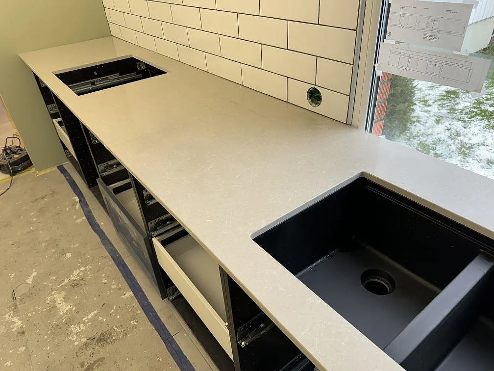 L formad köksbänkskiva i polerad Technistone Noble Ivory White kvartskomposit med svart diskho och hällöppning i ett kök i Falköping.