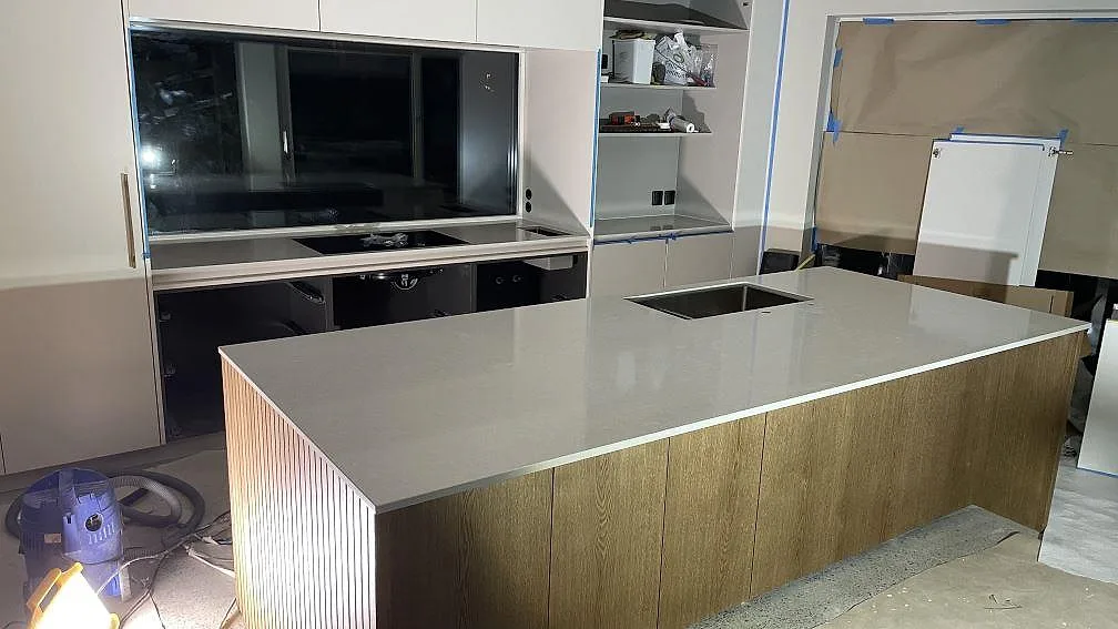 Köksbänkskiva i Technistone Noble Ivory White, polerad kvartskomposit, på köksö och bakre bänk i ett kök under montering i Frillesås.