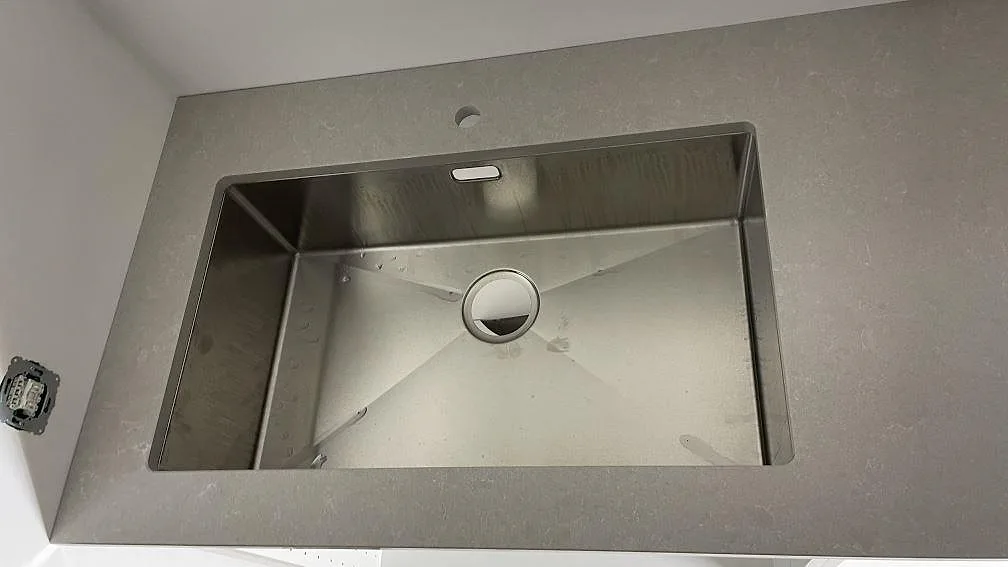 Sidobänk i polerad Technistone Noble Ivory White med rostfri diskho i ett kök under montering i Frillesås.