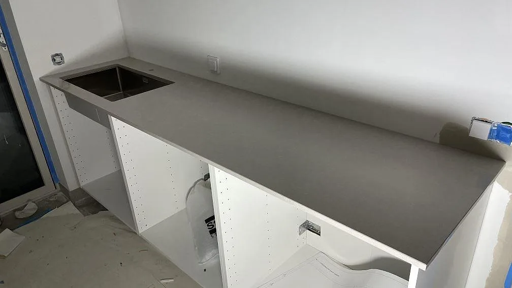 Lång väggbänk i Technistone Noble Ivory White med rostfri diskho och öppna köksstommar i Frillesås.