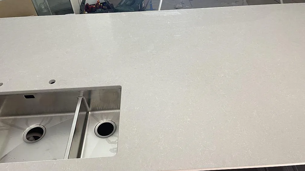 Närbild på ljus köksbänkskiva i Technistone Noble Ivory White med rostfri dubbelho under montering i Frillesås.
