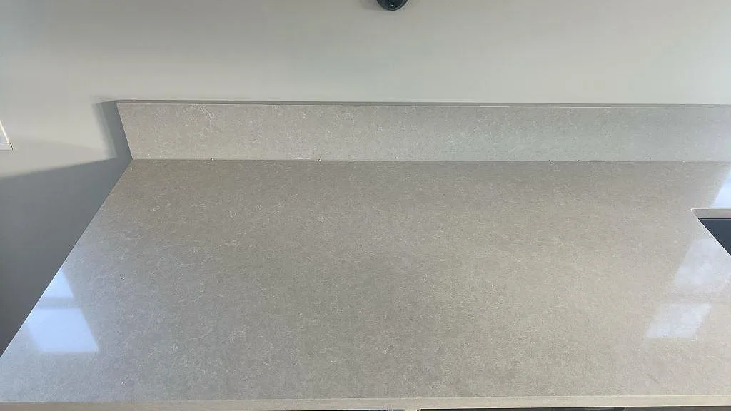 Närbild på den polerade ytan och den uppvikta stänkkanten i krämvit Technistone Noble Ivory White kvartskomposit i ett kök i Fritsla.