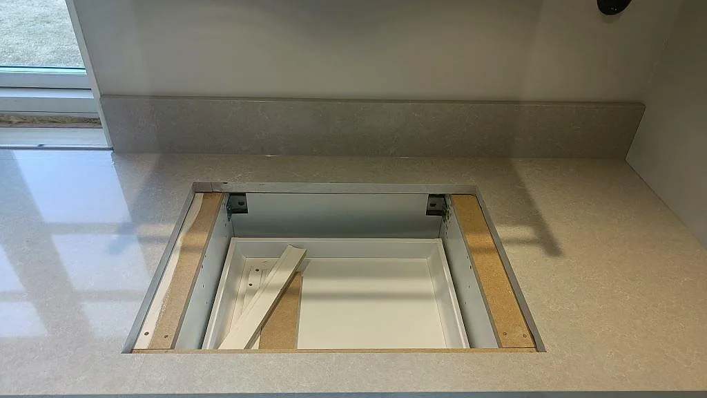 Urtag för häll i en bänkskiva av krämvit Technistone Noble Ivory White, med uppvikt stänkkant bakom, fotograferat under montering i Fritsla.