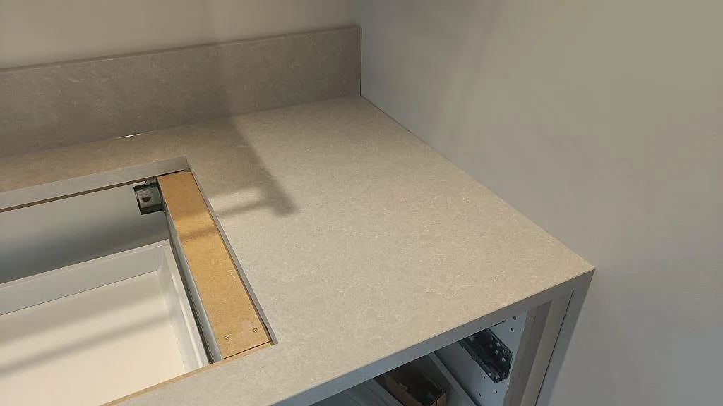 Hörn av den installerade köksbänkskivan i Technistone Noble Ivory White med uppvikt stänkkant, ljus kvartskomposit i ett kök i Fritsla.